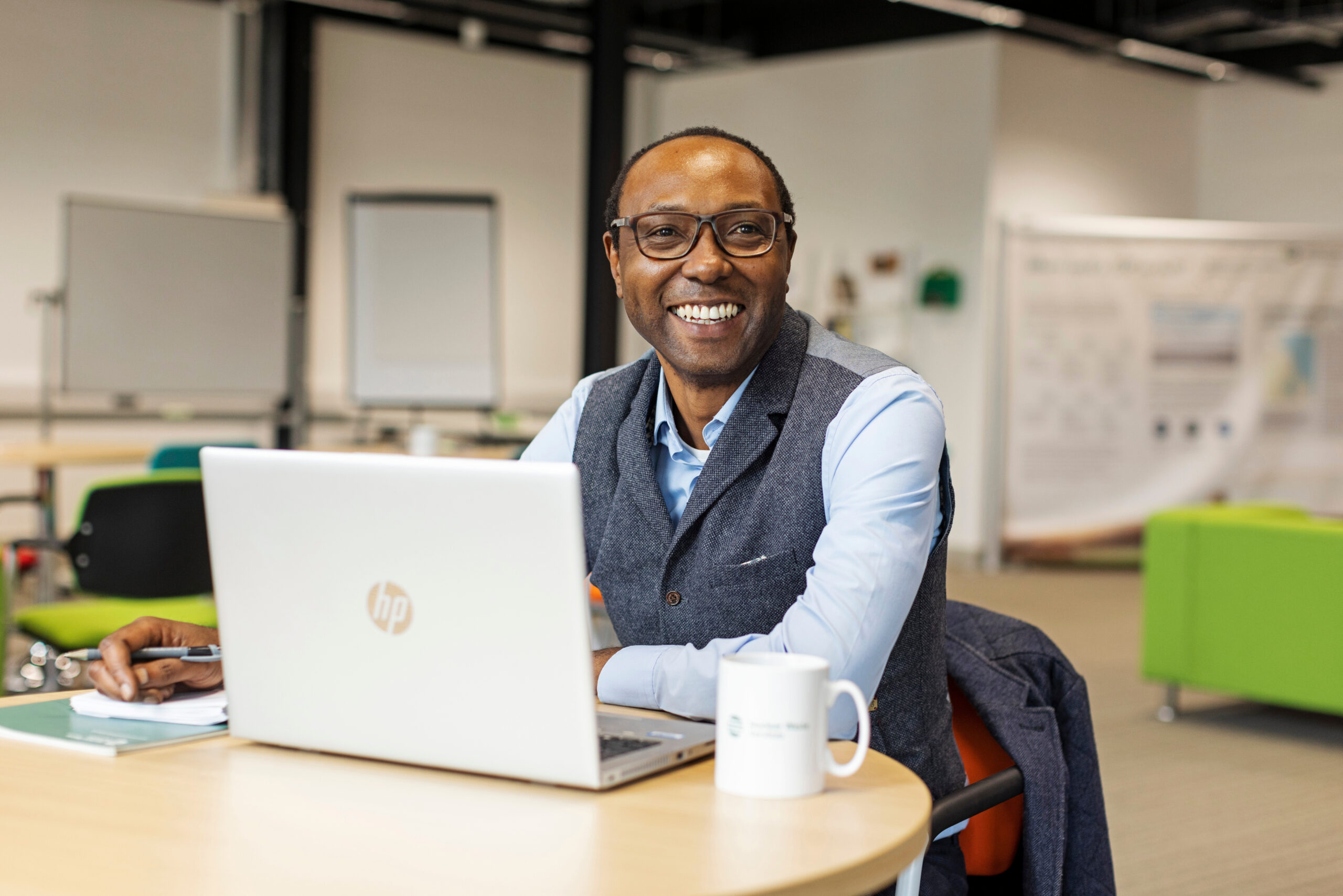 Man on laptop on table, smiling at camera